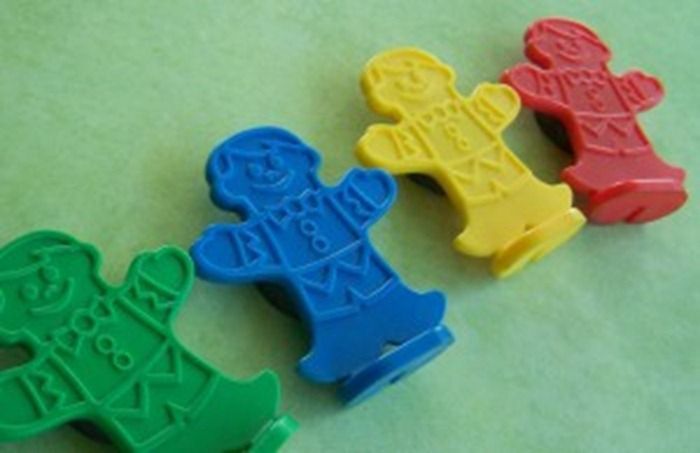 four meeples from the game Candy Land that resemble ginerbread cookies, each a different color: green, blue, yellow, red